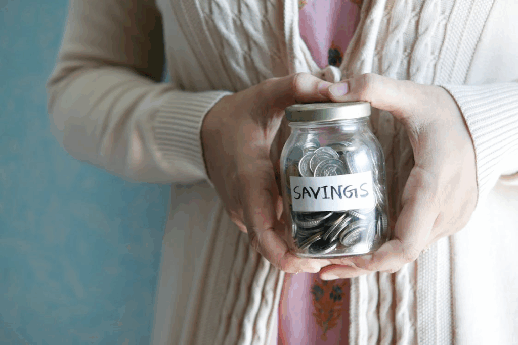 A glass jar filled with coins labeled “savings,” symbolizing the importance of saving money to build wealth.