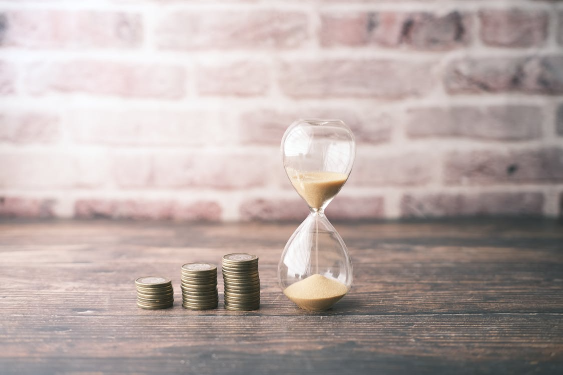 Stacks of coins beside an hourglass are a symbol of the power of compounding and how wealth grows over time.