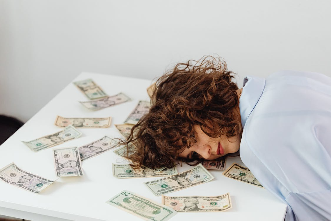 Exhausted woman with dollar bills, symbolizing financial stress and its toll on health.