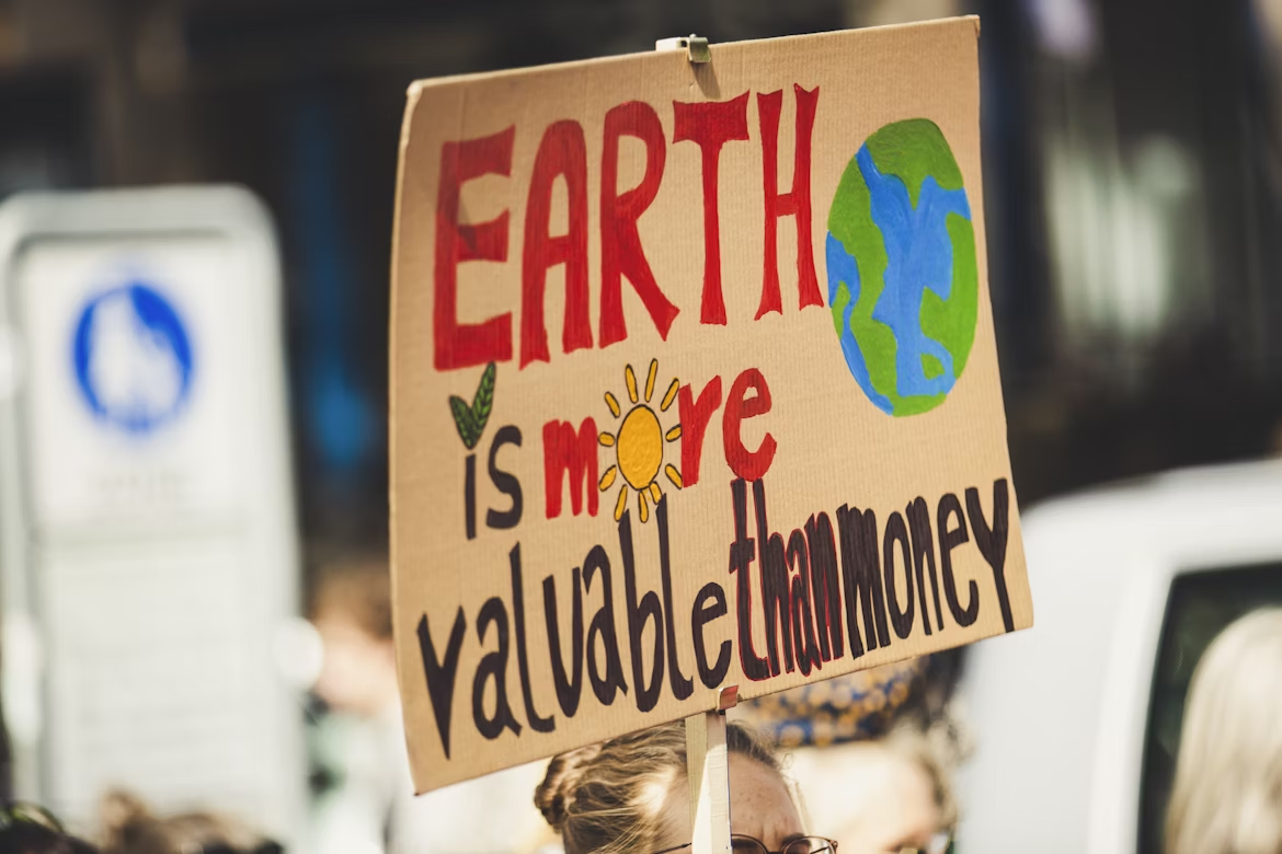 Sign reading “Earth is more valuable than money,” highlighting the link between climate change and money.