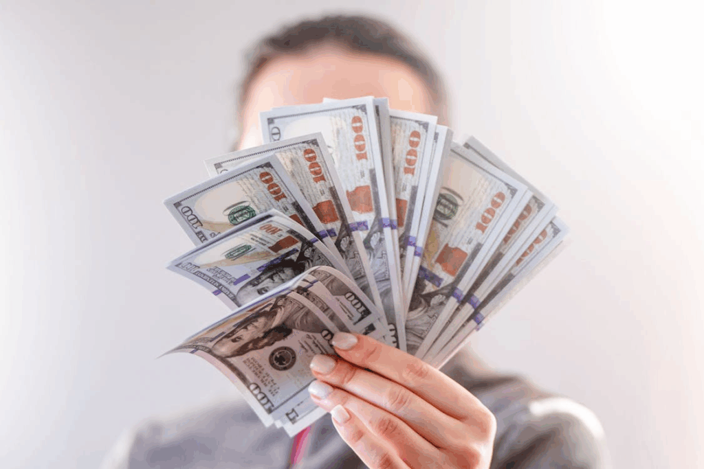 Person holding hundred-dollar bills, symbolizing liquidity and cash on hand.